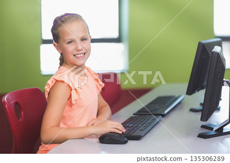 Elementary school girl typing on keyboard and moving mouse in computer lab with monitor, copy space 135306289