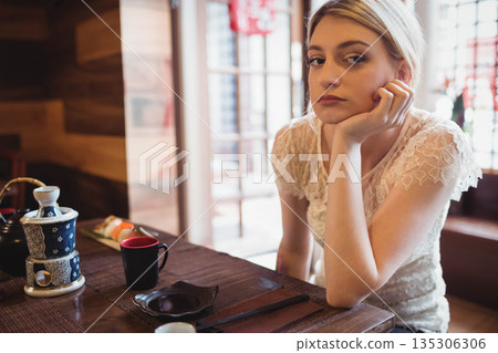 Woman resting head on hand at table in Japanese restaurant with ceramic teapot and sushi Woman resting head on hand at table in Japanese restaurant with ceramic teapot and sushi 135306306