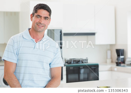 Man leaning on white countertop smiling gently in bright modern kitchen with bowl and coffee maker 135306343