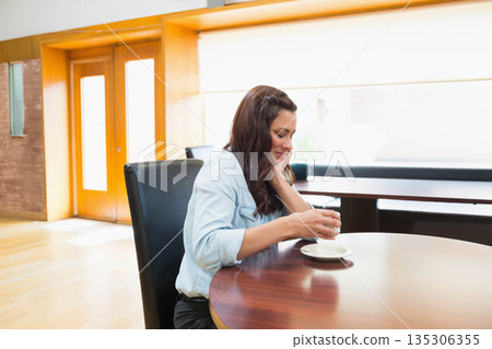Woman holding white ceramic cup above saucer at table in cafe wearing denim shirt, copy space Woman holding white ceramic cup above saucer at table in cafe wearing denim shirt, copy space 135306355