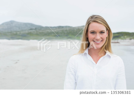 Woman standing and smiling on sandy coastal shoreline wearing white button-up shirt, copy space Woman standing and smiling on sandy coastal shoreline wearing white button-up shirt, copy space 135306381