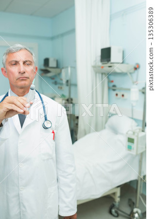 Male physician holding syringe and stethoscope at hospital room with bed and IV pole, copy space 135306389