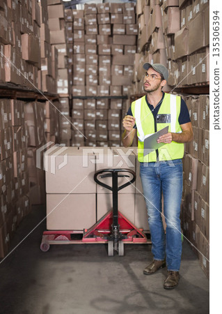 Male warehouse worker scanning pallet jack with tablet and stylus in warehouse aisle, copy space 135306394