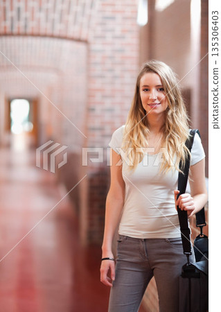 Female student standing in long brick corridor carrying black backpack over shoulder, copy space 135306403