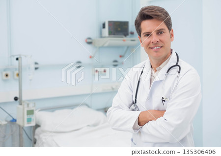 Middle aged doctor standing wearing lab coat in hospital patient room with stethoscope, copy space 135306406