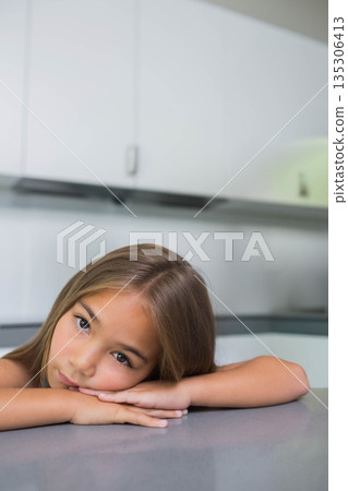 Child girl leaning forward on gray kitchen countertop, gazing into camera beside white cabinets Child girl leaning forward on gray kitchen countertop, gazing into camera beside white cabinets 135306413