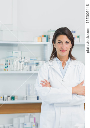 Female pharmacist in white lab coat standing arms crossed in pharmacy by pill bottles, copy space Female pharmacist in white lab coat standing arms crossed in pharmacy by pill bottles, copy space 135306448