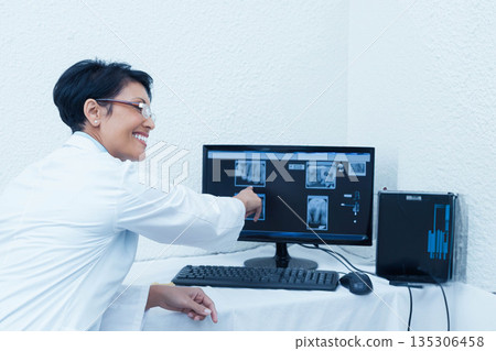 Female dentist pointing at x-rays on monitor in clinic with keyboard mouse, copy space 135306458