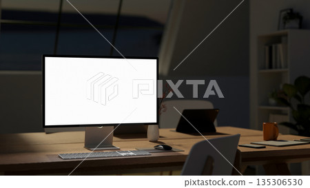 Blank screen computer and tablet with phone and coffee mug on wooden table in meeting room at night 135306530