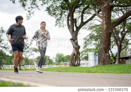 Asian woman and man in sportswear smiling talking during run or jogging together on pavement in park 135306570