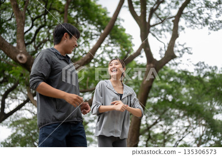 Asian man and woman in sportswear talking laughing at each other while running or jogging in park Asian man and woman in sportswear talking laughing at each other while running or jogging in park 135306573