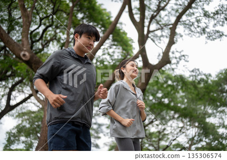 Asian man and woman in sportswear smiling as looking ahead while running or jogging together in park Asian man and woman in sportswear smiling as looking ahead while running or jogging together in park 135306574