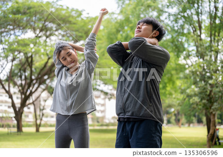 Asian man and a woman in sportswear standing and stretching arms and neck together in park courtyard Asian man and a woman in sportswear standing and stretching arms and neck together in park courtyard 135306596