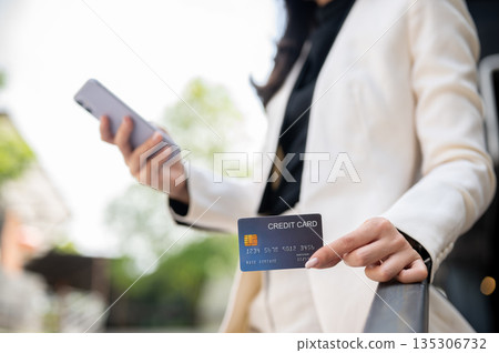Close up of office worker or businesswoman holding phone showing credit card while standing outside. 135306732
