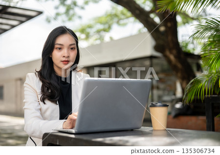Asian female office worker or businesswoman looking and working on laptop at table in cafe or garden Asian female office worker or businesswoman looking and working on laptop at table in cafe or garden 135306734