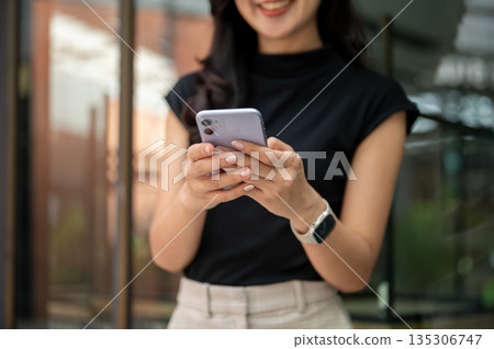 Asian student or female office worker holding phone typing or chatting outside cafe or coffee shop. 135306747