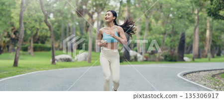 Young runner Asian woman jogging in park path, skinny fit in sports wear outfit leggings and top Young runner Asian woman jogging in park path, skinny fit in sports wear outfit leggings and top 135306917