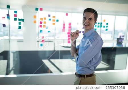 Adult man standing before glass partition with sticky notes near windows in office, copy space Adult man standing before glass partition with sticky notes near windows in office, copy space 135307036