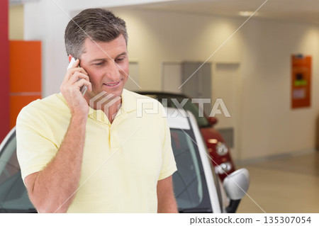 Senior man calling on smartphone and inspecting two-tone car with red panel in dealership showroom 135307054