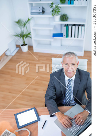 Middle-aged man wearing business attire working at desk in office using laptop computer, copy space Middle-aged man wearing business attire working at desk in office using laptop computer, copy space 135307055