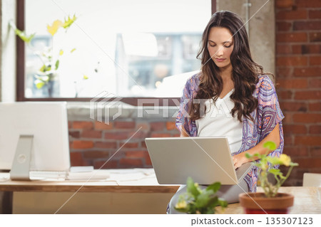 Woman working on silver laptop at loft-style workspace with wooden desk, potted plants, copy space Woman working on silver laptop at loft-style workspace with wooden desk, potted plants, copy space 135307123