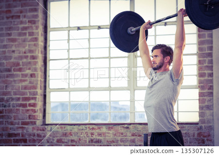Male athlete performing overhead barbell press in studio with brick wall and window, copy space Male athlete performing overhead barbell press in studio with brick wall and window, copy space 135307126