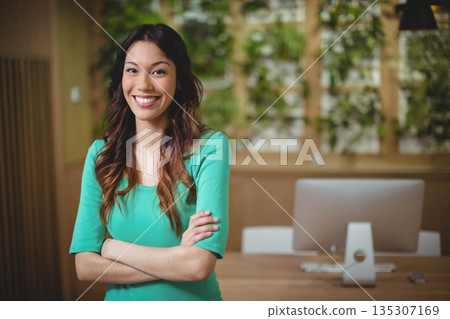 Female office professional smiling while crossing arms at desk with plant wall, copy space Female office professional smiling while crossing arms at desk with plant wall, copy space 135307169