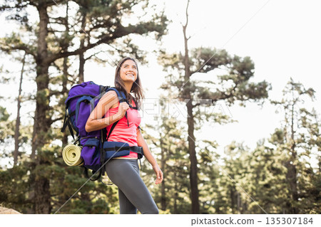 Female hiker standing on forest trail wearing coral tank with purple backpack and mat, copy space 135307184