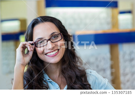 Woman holding eyeglass frame and adjusting fit while sitting at optical store display shelves Woman holding eyeglass frame and adjusting fit while sitting at optical store display shelves 135307185