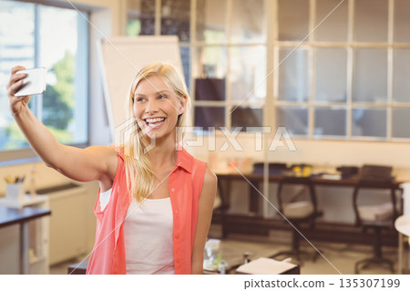 Woman standing in modern office near glass partition and flipchart holding smartphone and smiling 135307199