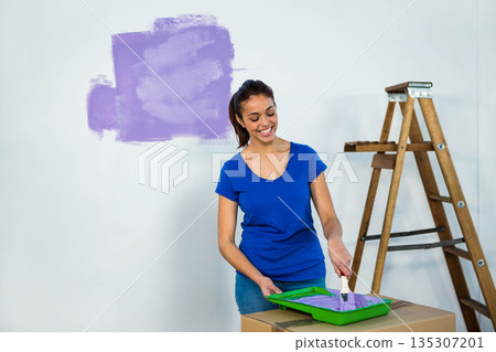 Woman painting white wall with purple paint at home using paintbrush and wooden stepladder 135307201