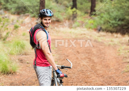 Male cyclist holding mountain bike on wooded trail wearing helmet and hydration pack, copy space Male cyclist holding mountain bike on wooded trail wearing helmet and hydration pack, copy space 135307229