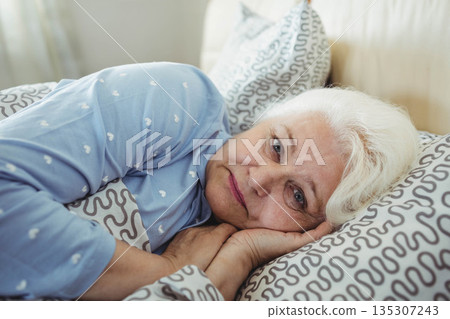 Senior woman wearing heart patterned pajamas lying in bed resting head on pillow 135307243