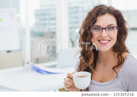 Woman holding white mug and working on laptop with folder at office desk, copy space Woman holding white mug and working on laptop with folder at office desk, copy space 135307258