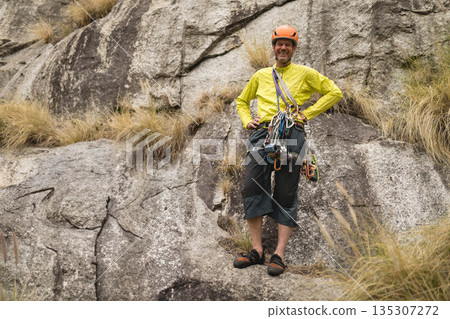 Senior male climber standing on rock cliff wearing yellow jacket and helmet with harness and rope Senior male climber standing on rock cliff wearing yellow jacket and helmet with harness and rope 135307272