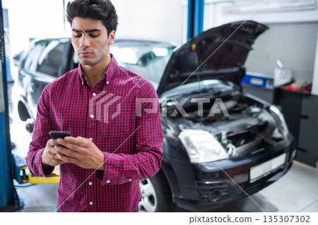 Asian man checking smartphone in repair garage with hatchback lift tool cabinet, copy space Asian man checking smartphone in repair garage with hatchback lift tool cabinet, copy space 135307302