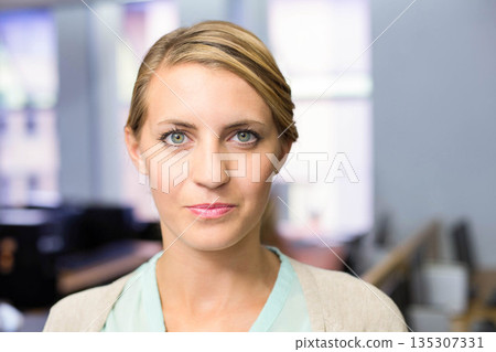 Professional woman standing in open office wearing cardigan over blouse with desks and windows 135307331