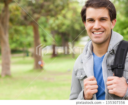 Male student standing in green park holding backpack straps and smiling at camera, copy space Male student standing in green park holding backpack straps and smiling at camera, copy space 135307356