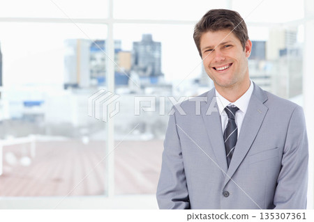 Middle-aged man wearing gray suit smiling in office before window revealing skyline, copy space Middle-aged man wearing gray suit smiling in office before window revealing skyline, copy space 135307361
