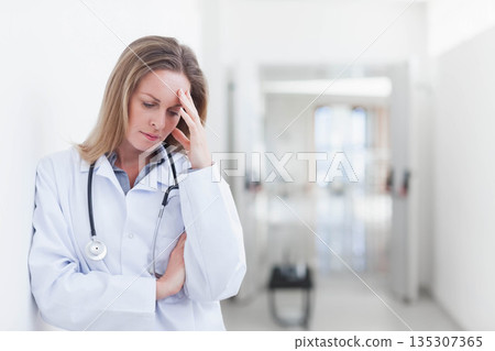 Female doctor standing in bright hospital corridor wearing lab coat and stethoscope, copy space Female doctor standing in bright hospital corridor wearing lab coat and stethoscope, copy space 135307365