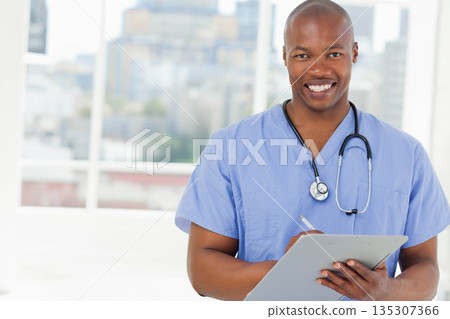 African American male doctor writing notes on clipboard with stethoscope in clinic room, copy space 135307366