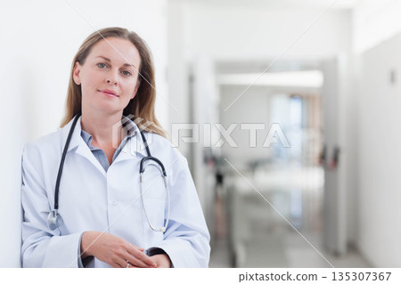 Female doctor standing in hospital hallway wearing lab coat and stethoscope, copy space 135307367