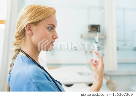 Female medical professional inspecting syringe in clinic with stethoscope near bed, copy space Female medical professional inspecting syringe in clinic with stethoscope near bed, copy space 135307369