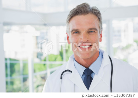 Male doctor standing by glass windows at clinic wearing white coat, stethoscope, copy space Male doctor standing by glass windows at clinic wearing white coat, stethoscope, copy space 135307387