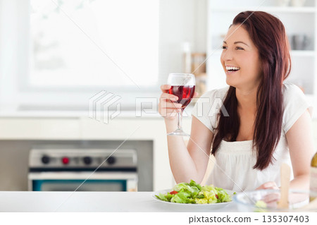 Woman sipping red wine while eating fresh salad at modern kitchen countertop, copy space Woman sipping red wine while eating fresh salad at modern kitchen countertop, copy space 135307403