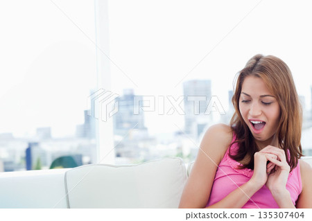 Woman wearing pink top sitting on sofa near large window gazing at city skyline, copy space Woman wearing pink top sitting on sofa near large window gazing at city skyline, copy space 135307404