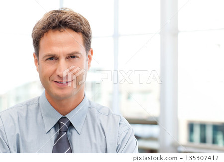 Businessman wearing light blue shirt with striped tie sitting in office by large glass windows 135307412
