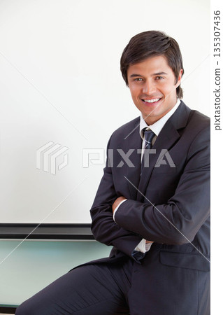 Businessman in suit leaning against ledge under whiteboard at office smiling at camera copy space Businessman in suit leaning against ledge under whiteboard at office smiling at camera copy space 135307436