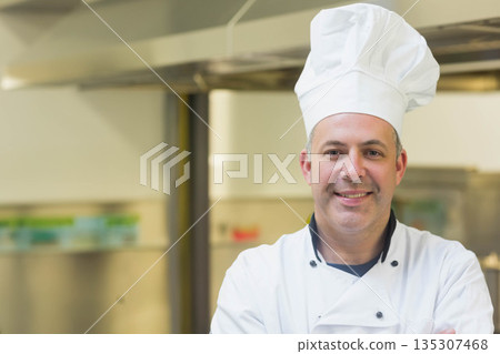 Male chef wearing white chef jacket and hat standing under vent hood in kitchen, copy space 135307468