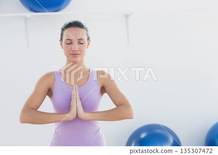 Female in lavender top closing eyes pressing palms in yoga studio with blue exercise balls Female in lavender top closing eyes pressing palms in yoga studio with blue exercise balls 135307472